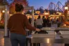 An anonymous visitor places a small plain bag on a generic amusement-park security table before a fall evening event.