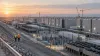 Engineers walking beside a vast data-center campus with cooling systems, electrical equipment and construction cranes at dawn