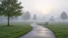 Illustrative view of a quiet municipal park path and distant playground in morning fog.