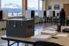 A sealed ballot box inside an Alaska polling place with snowy mountains visible through the windows