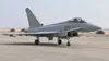 AI-generated illustration of an unmarked grey canard-delta fighter jet parked on an arid airfield; not a photograph of the announced RAF deployment.