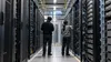 Two data-center engineers inspect unbranded server racks in a high-density computing facility.