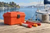 AI-generated illustration of unlit marine flares and a safety container beside a sailboat; not a collection-event photograph.