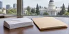 AI-generated illustration of unmarked envelopes and a folder on an office desk with civic architecture beyond; not actual ballots, evidence or an arrest scene.