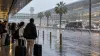 Os viajantes com bagagem abrigam-se da chuva forte à porta de um terminal de aeroporto.