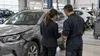 An insurance assessor and repair technician review vehicle damage on a tablet in a collision repair facility.