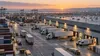 Illustrative view of an intermodal freight logistics hub with trucks, containers and warehouses at dawn.