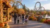 Families walking through an autumn-decorated Northern California amusement park beneath a looping roller coaster