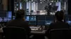 Two television production professionals seated in a generic broadcast control room overlooking a studio camera