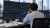 Um analista financeiro estuda gráficos do mercado obrigacionista em vários monitores num escritório moderno.