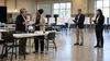 Local election administrators prepare a polling place while two neutral observers take notes nearby.