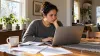 An adult borrower reviews financial information on a laptop at a dining table in a naturally lit home