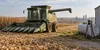 AI-generated illustrative scene of an unbranded combine harvester beside a farm fuel tank and harvested cornfield; not an actual aid recipient.