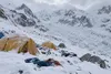 Illustrative editorial image of an empty snow-covered Himalayan expedition camp beneath steep mountain slopes