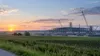 Rural Iowa fields beside a generic steel-plant construction site under an early morning sky.