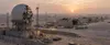 Illustrative view of a damaged radar enclosure and aircraft hangars at a desert military base at dawn
