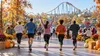 Recreational runners cross a generic finish area inside an autumn-decorated amusement park on a bright morning.