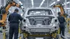 Anonymous autoworkers stand beside an unbranded vehicle body on a modern Michigan assembly line in an editorial illustration.