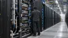 An engineer inspects liquid-cooled, unbranded computer racks inside a modern data center.