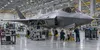 Technicians inspect an unmarked next-generation fighter aircraft inside a modern aerospace hangar.