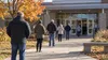 Anonymous election observers and state staff stand outside a generic Minnesota polling place in an illustrative editorial scene.