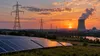 Transmission lines cross Missouri farmland at dusk beside a distant power station and solar panels, illustrating the state energy policy debate.