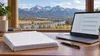 Blank benefit forms and a laptop with abstract checkboxes sit on a desk overlooking Montana mountains, illustrating Medicaid compliance paperwork.