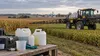 Illustrative Nebraska cropland with a farm sprayer and unbranded agricultural supply containers.