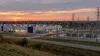 Um grande centro de dados e uma subestação elétrica erguem-se perto de uma comunidade do Midwest americano ao pôr-do-sol.