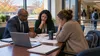 School administrators and a parent review enrollment and budget documents in a school meeting room.