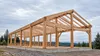 AI-generated editorial illustration of an unfinished timber building frame in a generic Oregon setting; not a photograph of a particular employer or September construction activity.