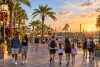 Visitors walk along an unbranded palm-lined Central Florida entertainment promenade in warm evening light
