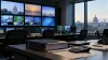 Uma sala de monitorização de televisão vazia, com edifícios governamentais visíveis para lá das janelas, documentos orçamentais e uma calculadora em cima da secretária.