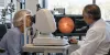 An older patient undergoes retinal imaging while an ophthalmologist reviews the examination in an eye clinic.