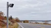 AI-generated editorial illustration of a generic roadside camera beside an empty New England road; not a photograph of a Rhode Island installation or a specific vendor’s device.
