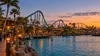 A coastal Southern California theme park with a roller coaster and waterfront midway at twilight