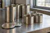 AI-generated illustrative photograph of unbranded metal food cans and lids on a workbench; not a Silgan or Trivium facility.