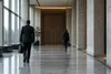 Two officials walk through a quiet government corridor toward closed meeting-room doors, illustrating confidential diplomacy.