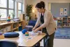 An education aide arranges adaptive learning materials in an empty classroom, illustrating special-education staffing needs.