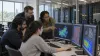 Investigadores universitários colaboram em estações de trabalho junto a bastidores de servidores num laboratório de informática académico.