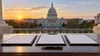 Three document folders and a fountain pen on a desk overlooking the U.S. Capitol at sunrise.
