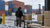 A trade-compliance professional inspects unlabeled cartons at a cargo terminal, illustrating scrutiny of import tariffs.