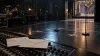 An illustrative empty music stage with two microphone stands and sealed submission envelopes on a mixing console.