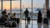 Travelers with luggage waiting inside a Gulf-region airport terminal beside a parked passenger aircraft at dawn