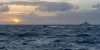 Vista ilustrativa de uma pequena lancha rápida e de um navio patrulha ao longe, no Mar das Caraíbas, ao amanhecer