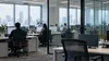 A modern office with several occupied workstations and empty desks in the foreground.