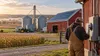 Farmer reviewing electrical equipment beside a barn with rooftop solar panels