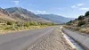 AI-generated editorial illustration of a generic rural mountain road beside a drainage channel in Utah-like terrain; not a specific damaged road or a documented recovery scene.