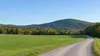 Illustrative Vermont farm field and forested hill with a repaired gravel access lane after past weather damage