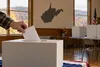 An unmarked ballot entering a plain ballot box in an Appalachian community polling place.